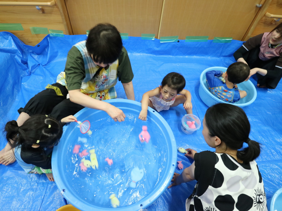 大きいたらいに魚を浮かべて遊ぶ幼児と、小さいたらいの水に浸かっている幼児