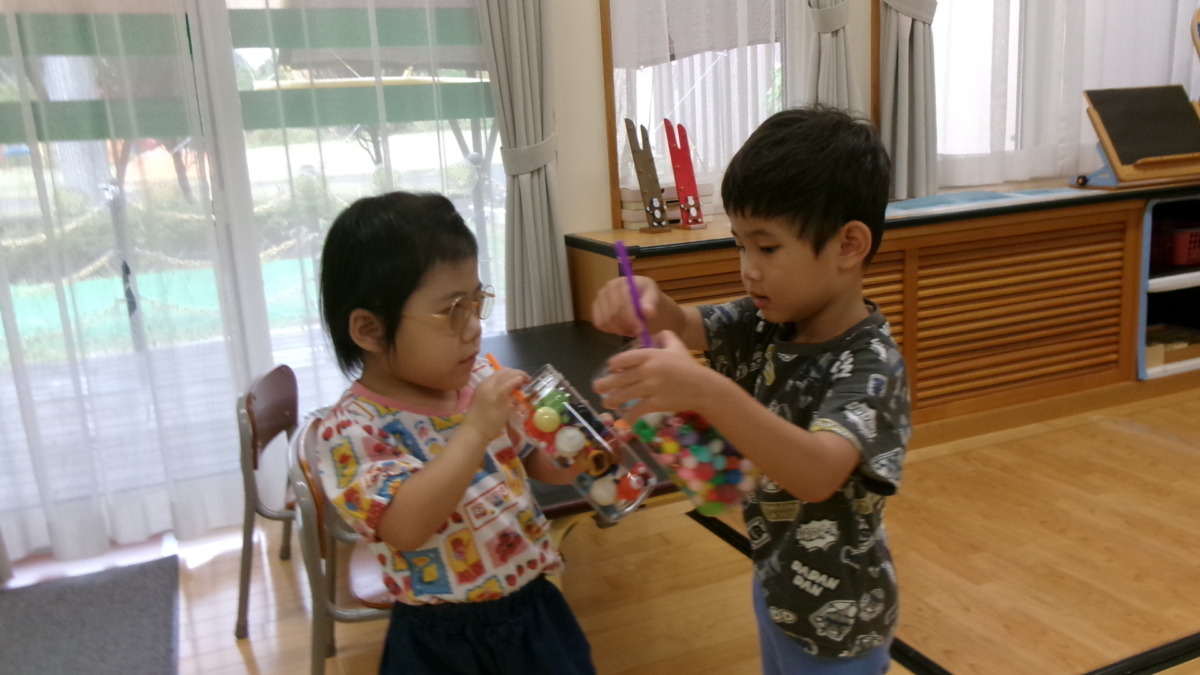透明な容器の中にカラフルなボールを詰め、ジュースのようにして乾杯する幼児2名