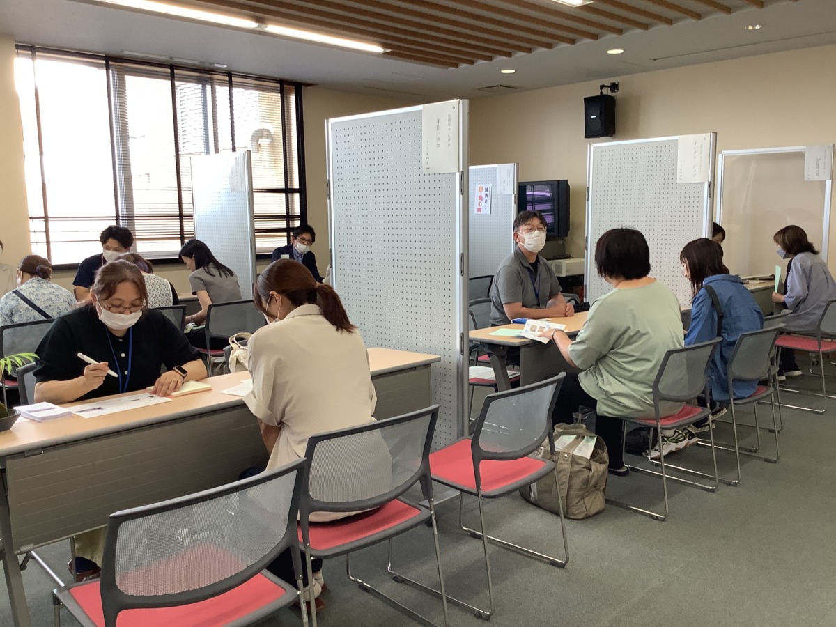 パーテーションで事業所ごとにテーブルを区切り、保護者が事業所の方と向かい合う形で話をしている様子。