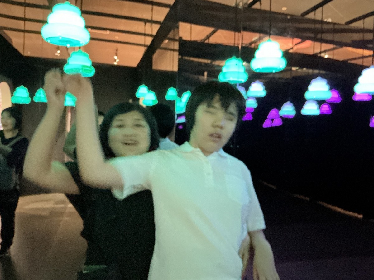 暗い部屋に、内部からネオンライトで照らされたうんこの模型がたくさんつるされており、その中を歩いている生徒