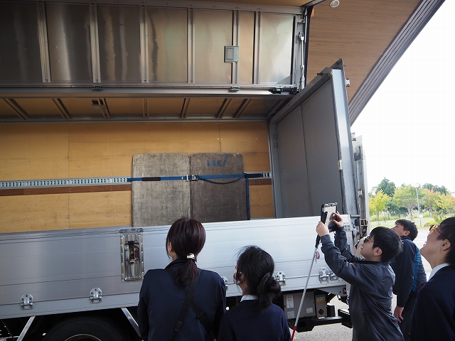 トラックの荷台が横から上にかけて開いている様子を眺めている児童生徒。